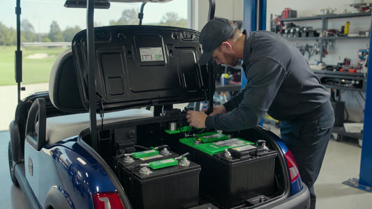 Golf cart maintenance technician inspecting battery compartment showing lead-acid and lithium battery safety comparison in a professional fleet environment.
